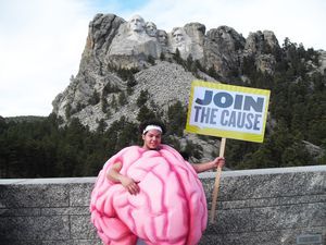 A man in a brain costume is holding a sign that says join the cause