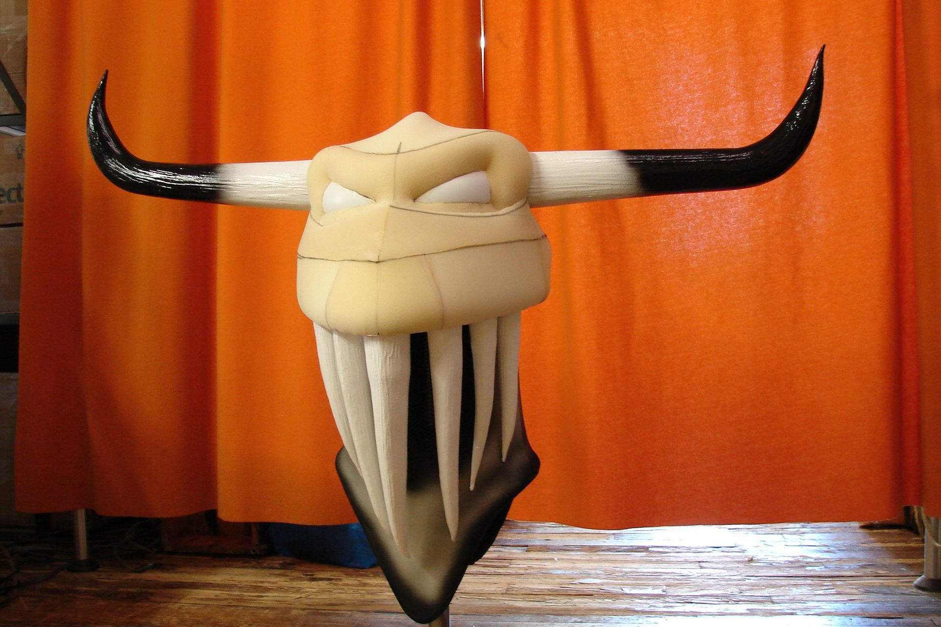 A statue of a bull 's head is hanging from a pole in front of an orange curtain