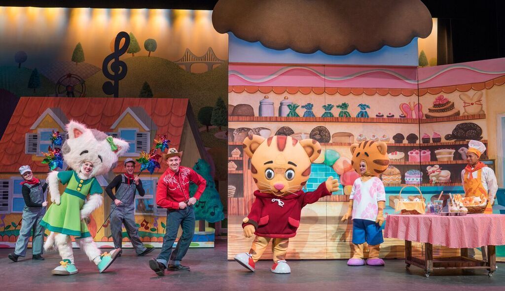 A group of mascots are dancing on a stage in front of a bakery.