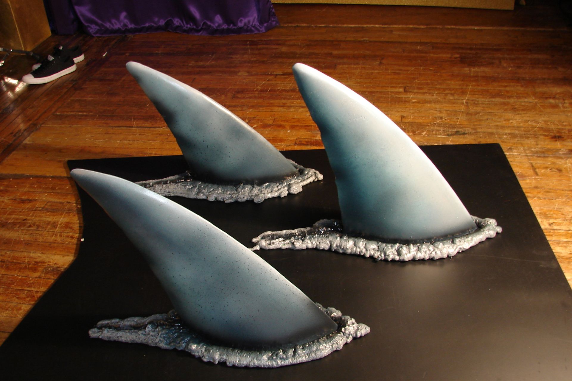 Three shark fin sculptures are sitting on a black mat