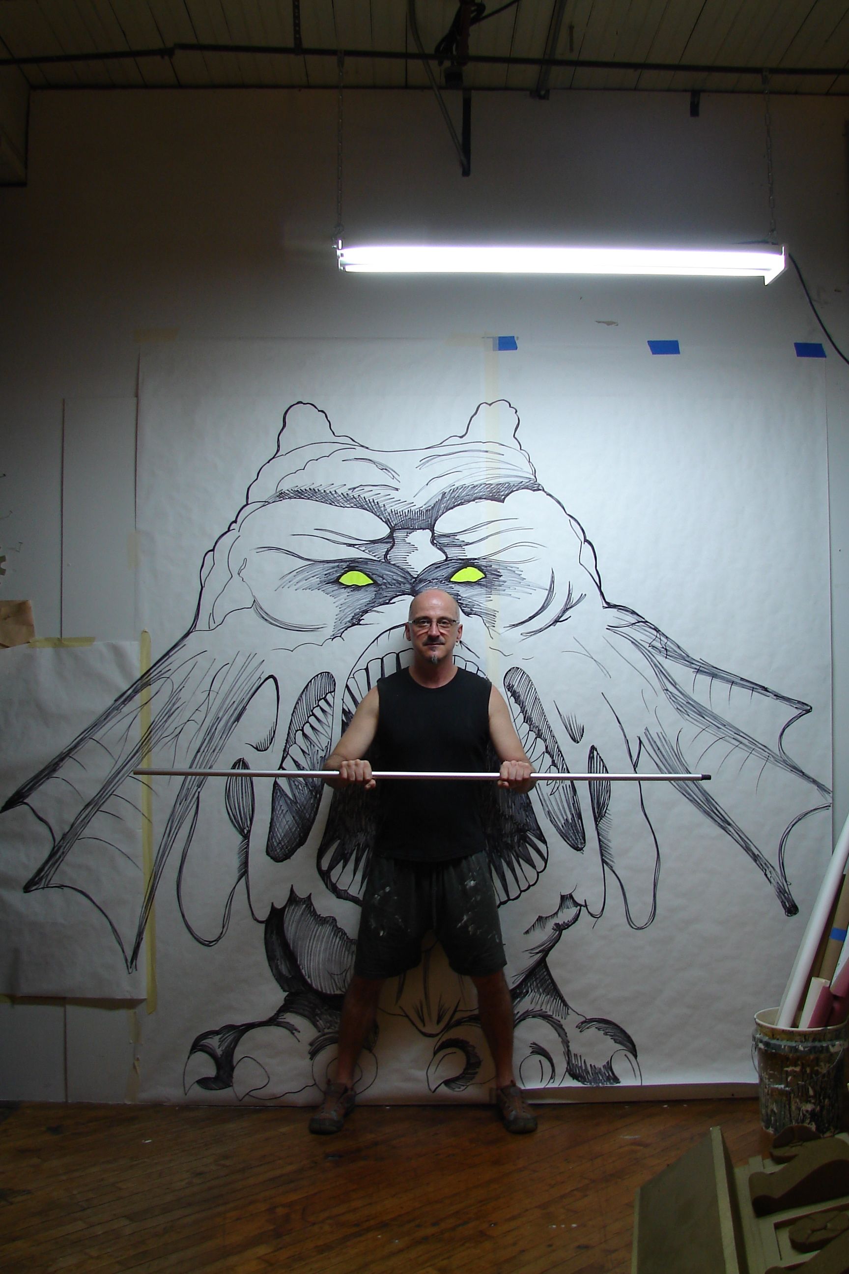 A man is standing in front of a painting of a monster holding a barbell.