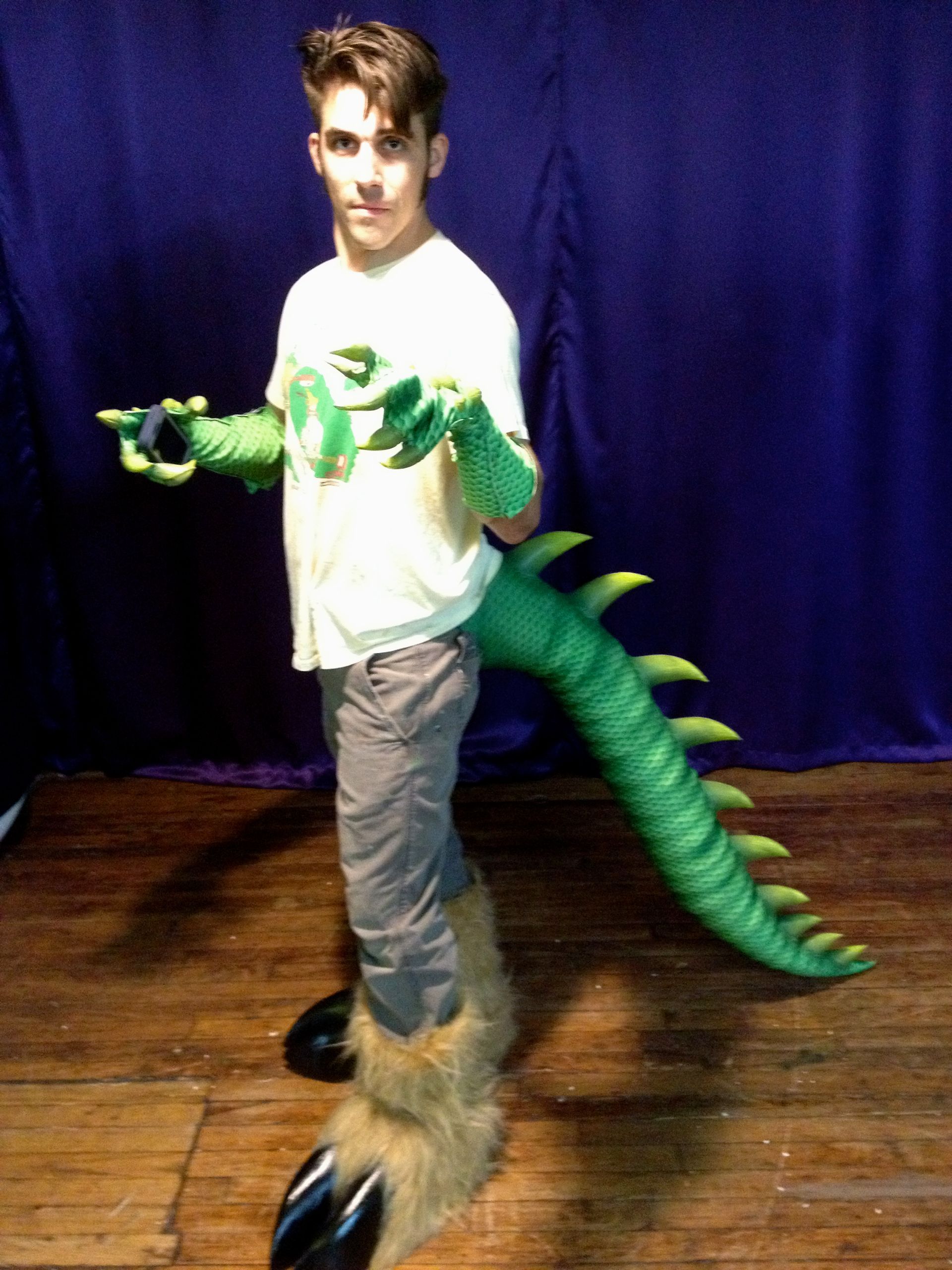 A boy in a dinosaur costume is standing on a wooden floor