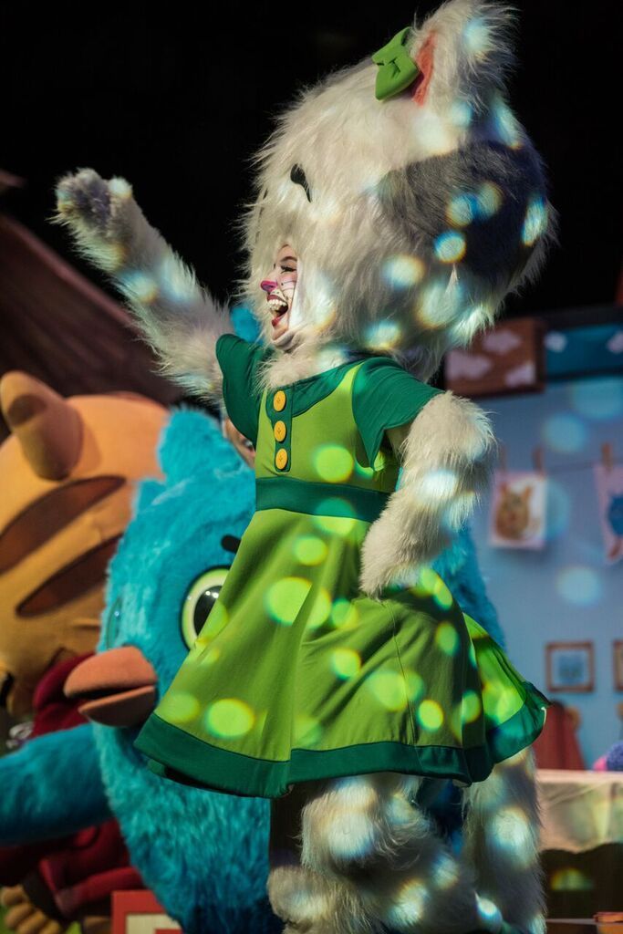 A stuffed cat in a green dress is standing next to a stuffed bird.