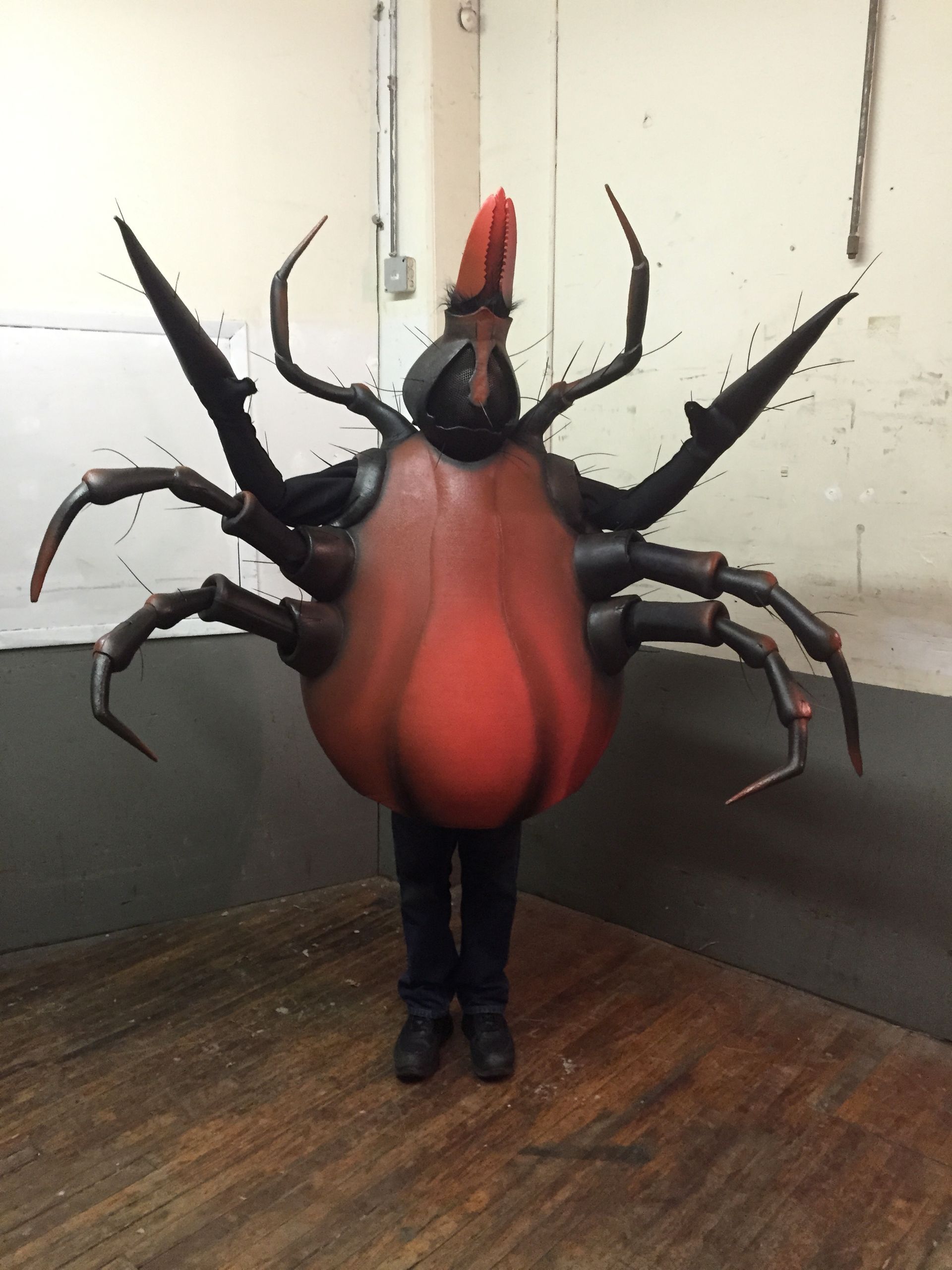 A person dressed in a red spider costume is standing on a wooden floor