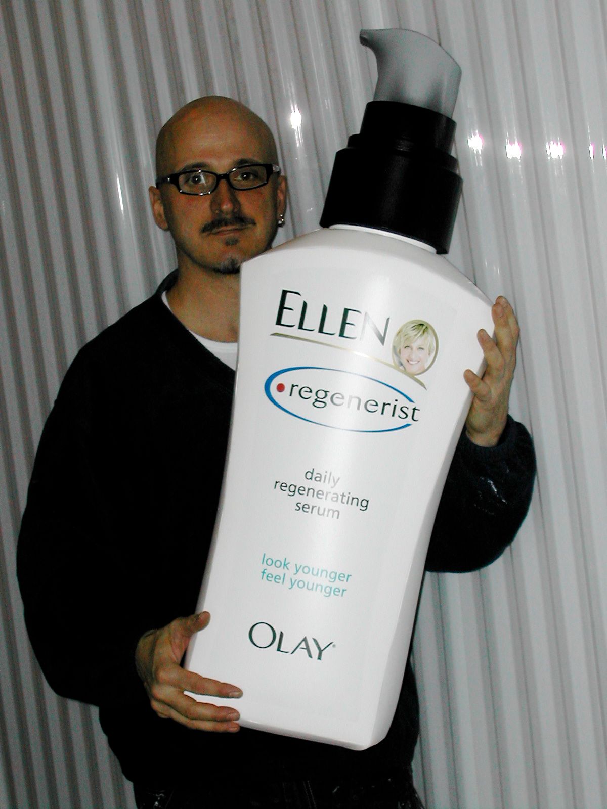 A man is holding a large bottle of ellen 's regenerist lotion