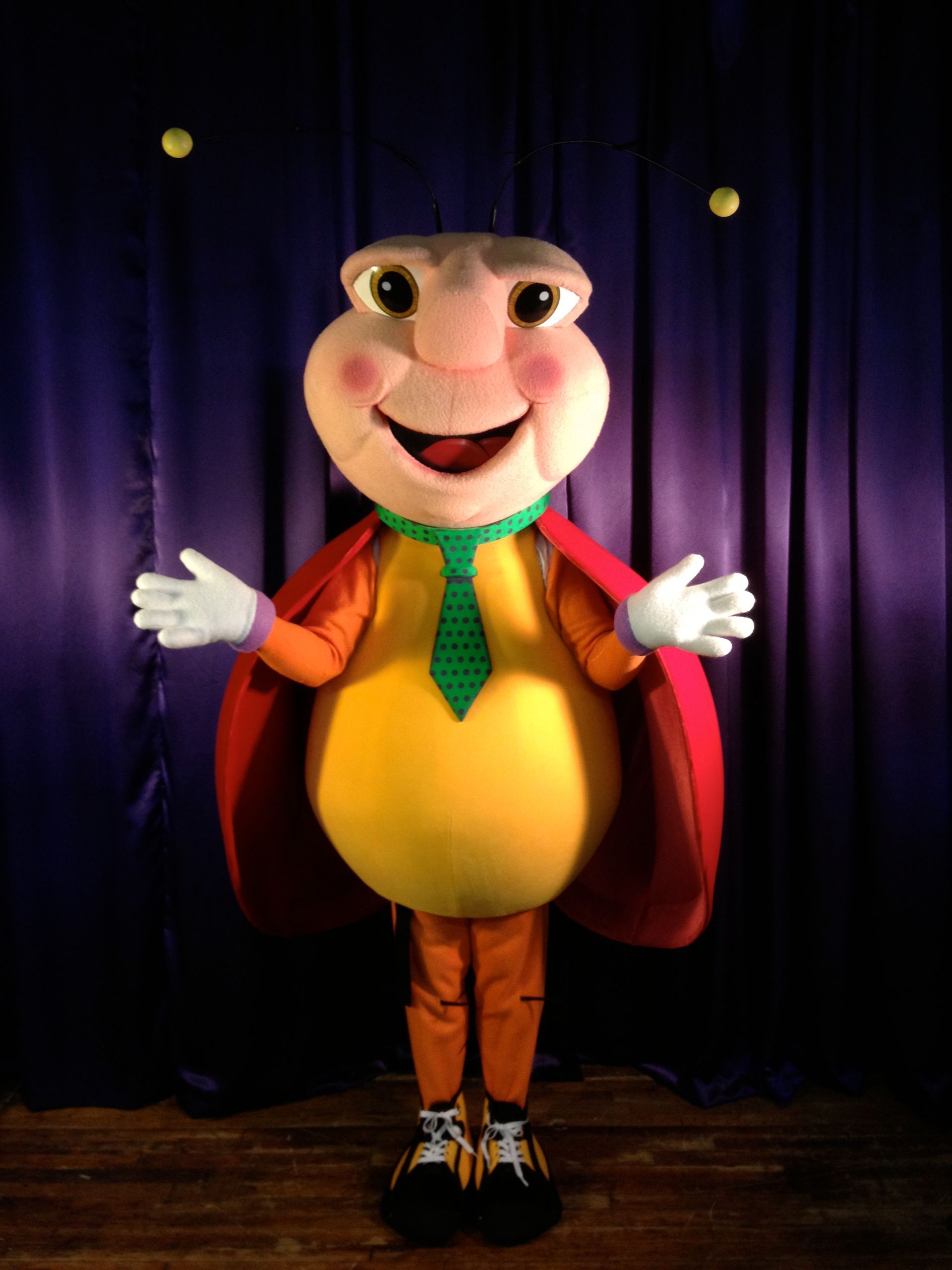 A ladybug mascot is standing in front of a purple curtain