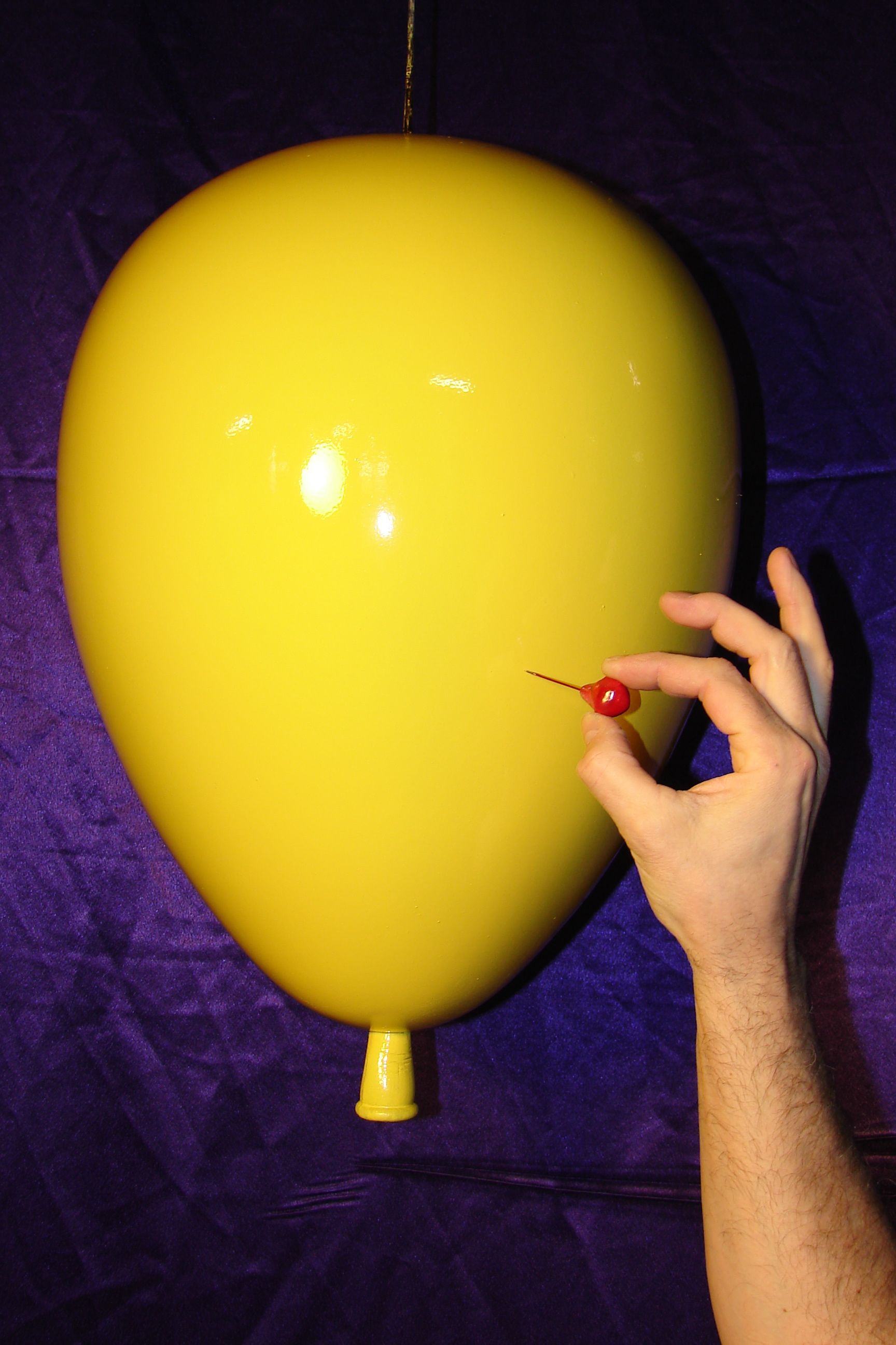 A person is holding a cherry in front of a yellow balloon