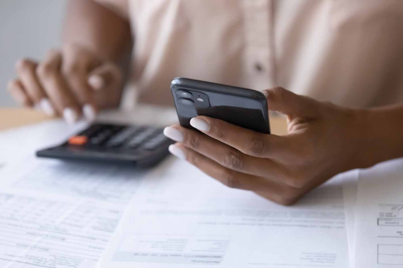 A woman is using a calculator while holding a cell phone.
