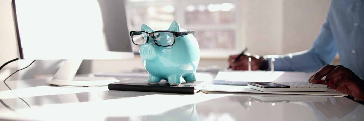 A blue piggy bank with glasses is sitting on a desk.