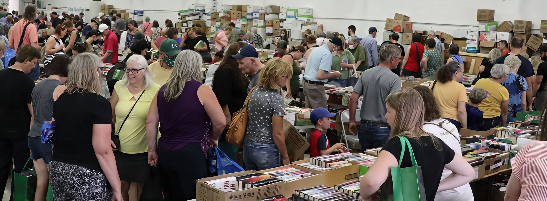 Crowd shopping at a flea market, indoor setting with many tables and boxes of merchandise.