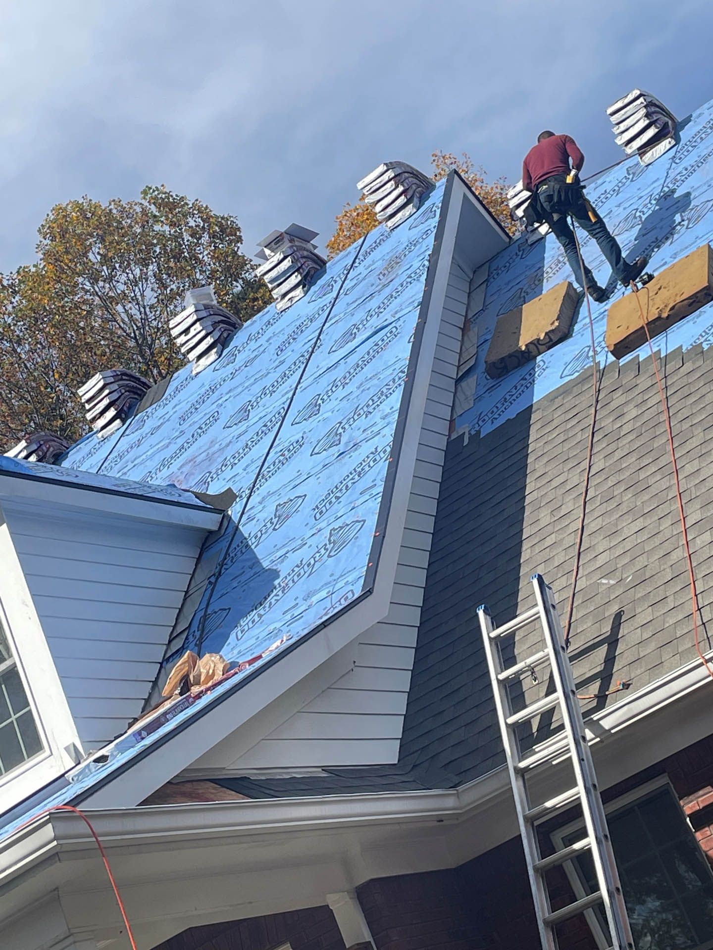 A man is working on the roof of a house with a ladder.