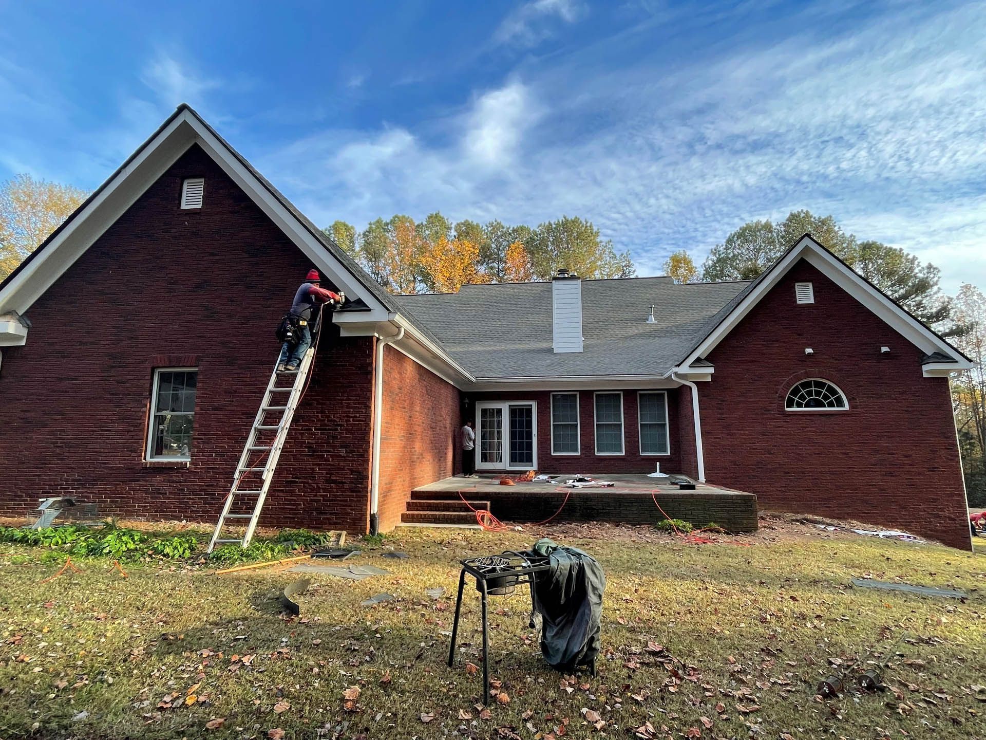 A man is standing on a ladder in front of a large brick house.