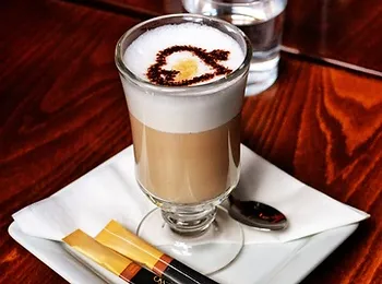 a glass of cappuccino on a white plate with sugar sticks and a spoon