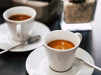 two cups of espresso on saucers with spoons on a table .