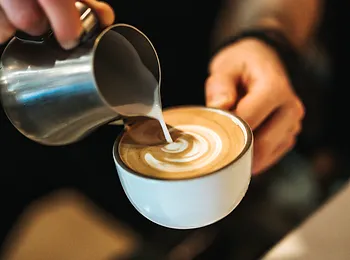 a person is pouring milk into a cup of cappuccino .