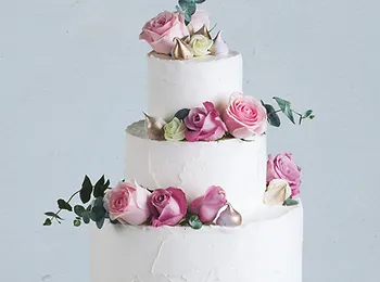a three tiered wedding cake decorated with pink roses and eucalyptus leaves .