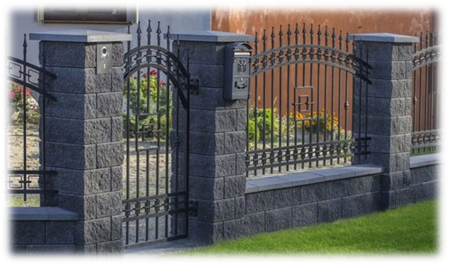 Una recinzione in pietra con un cancello in ferro battuto e una cassetta postale