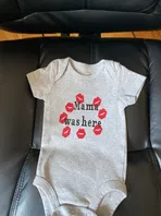A baby onesie with red kisses on it is sitting on a chair.