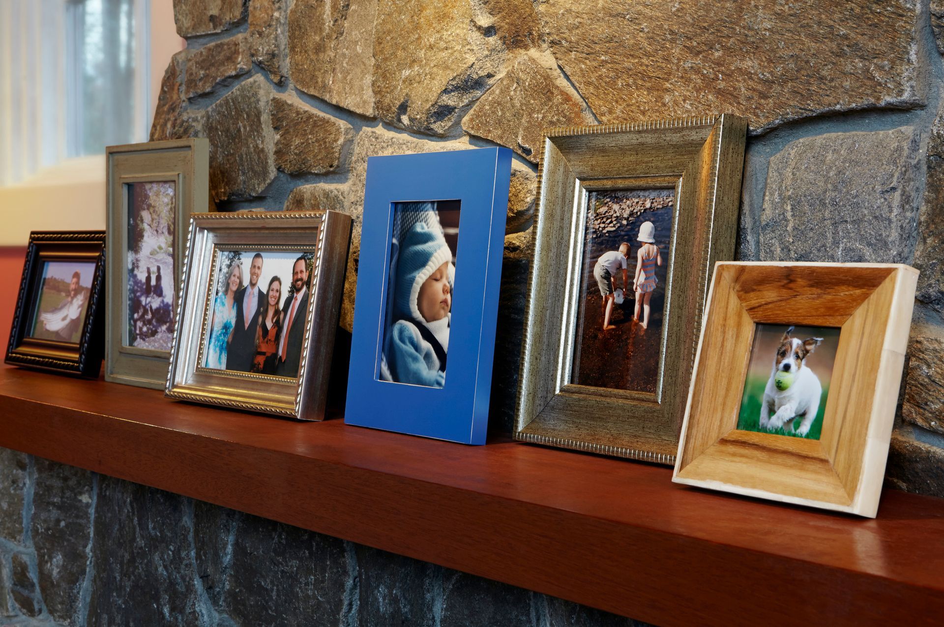 A row of picture frames on a mantle with a stone wall in the background