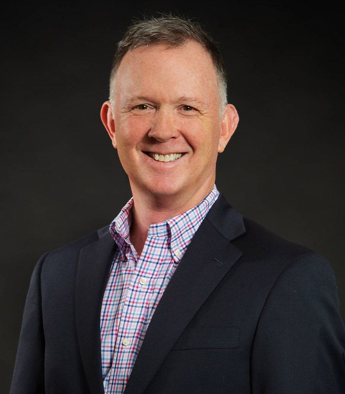 A man in a suit and plaid shirt is smiling for the camera.