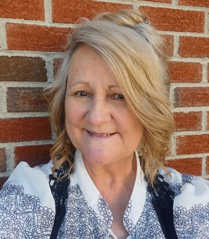 A woman is smiling in front of a brick wall