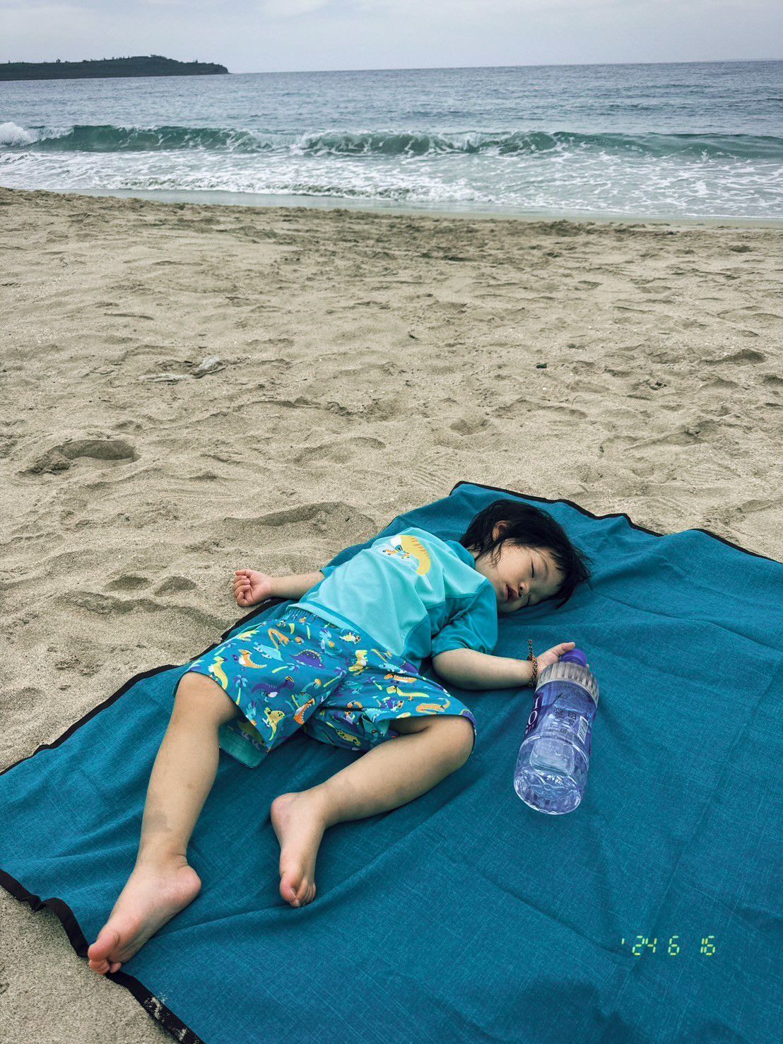 一個人躺在沙灘上的碧藍色毯子上睡著了,手裡拿著一個透明的水瓶,靠近海浪。