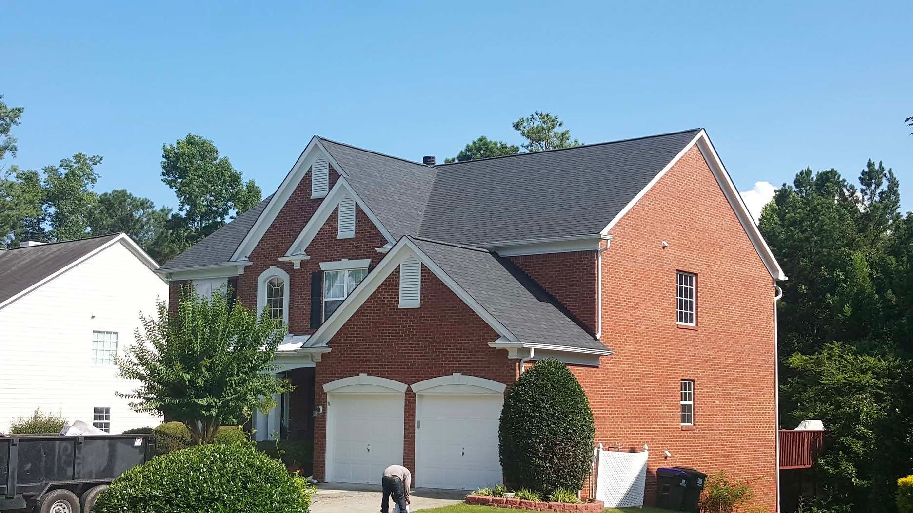 A brick house with a black roof and white garage doors