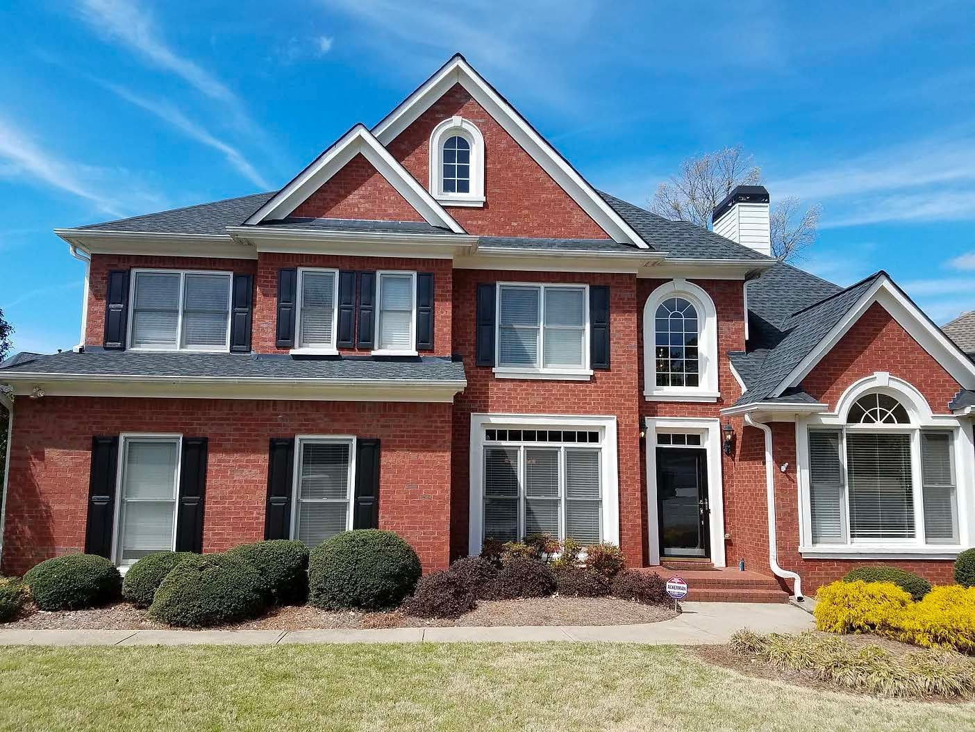 A large brick house with black shutters and a blue sky in the background.