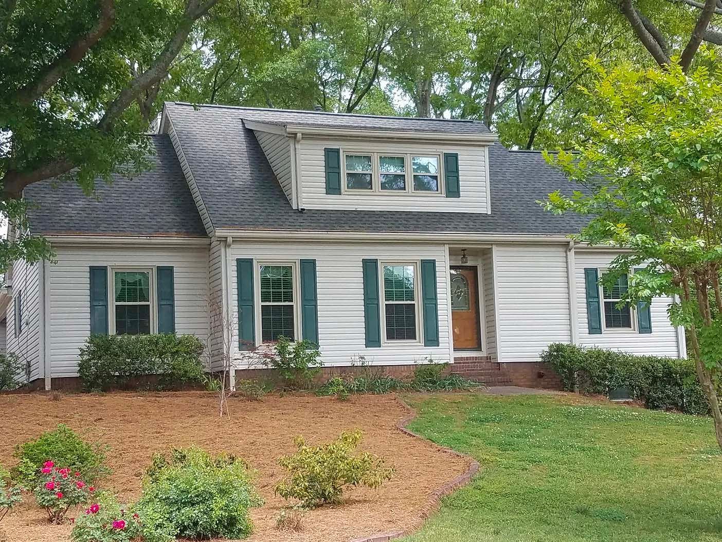 A white house with green shutters and a black roof