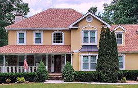 A large yellow house with a red roof and a large porch.