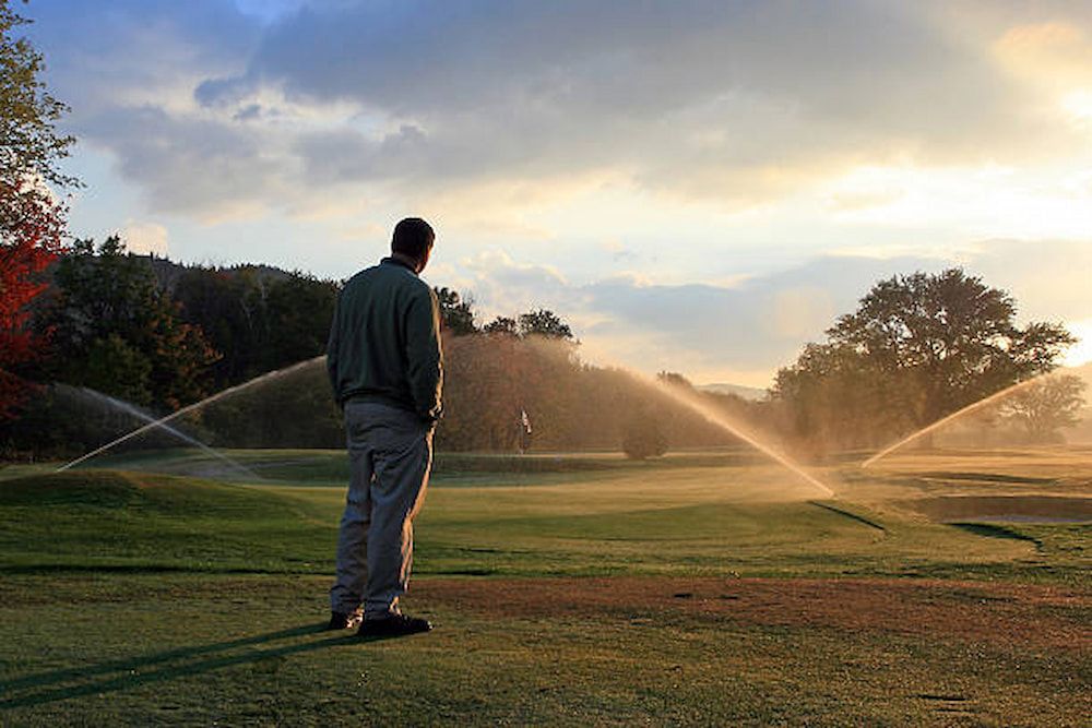 A Man Is Standing In Front Of A Sprinkler On A Golf Course — Southern Turf Supplies In Bega, NSW