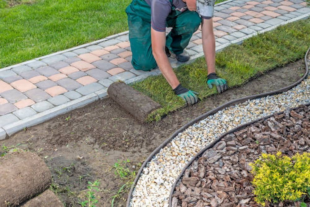 A Man Is Kneeling Down To Roll Out Grass In A Garden — Southern Turf Supplies In Termeil, NSW