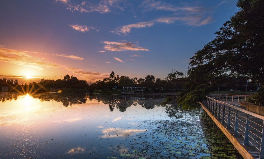 The Sun Is Setting Over A Lake With A Bridge In The Foreground — Southern Turf Supplies In Eden, NSW