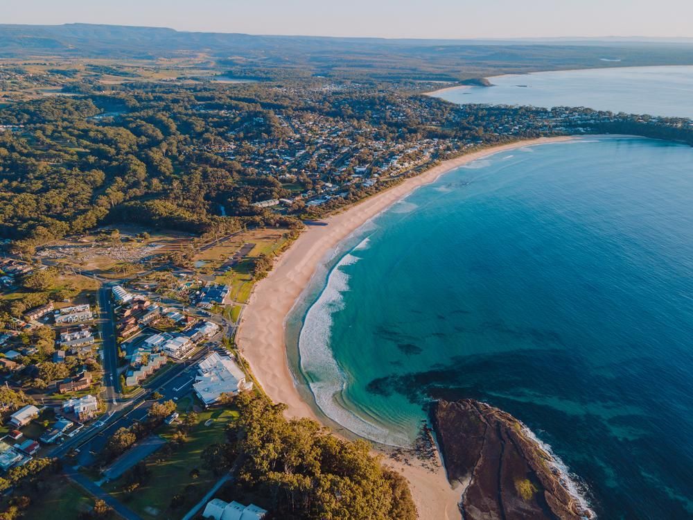 An Aerial View Of A Beach And A Body Of Water With A City In The Background — Southern Turf Supplies In Mollymook, NSW