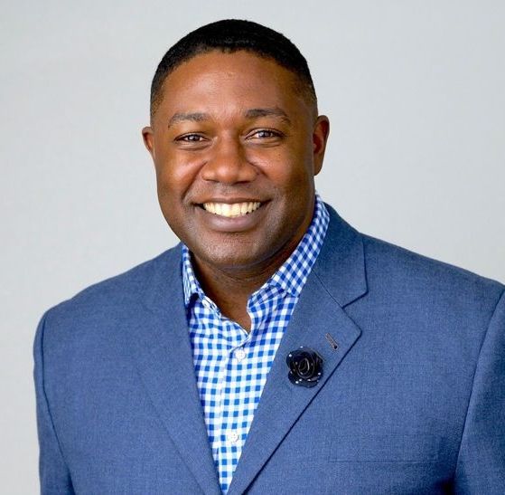 A man in a blue suit and plaid shirt is smiling for the camera.