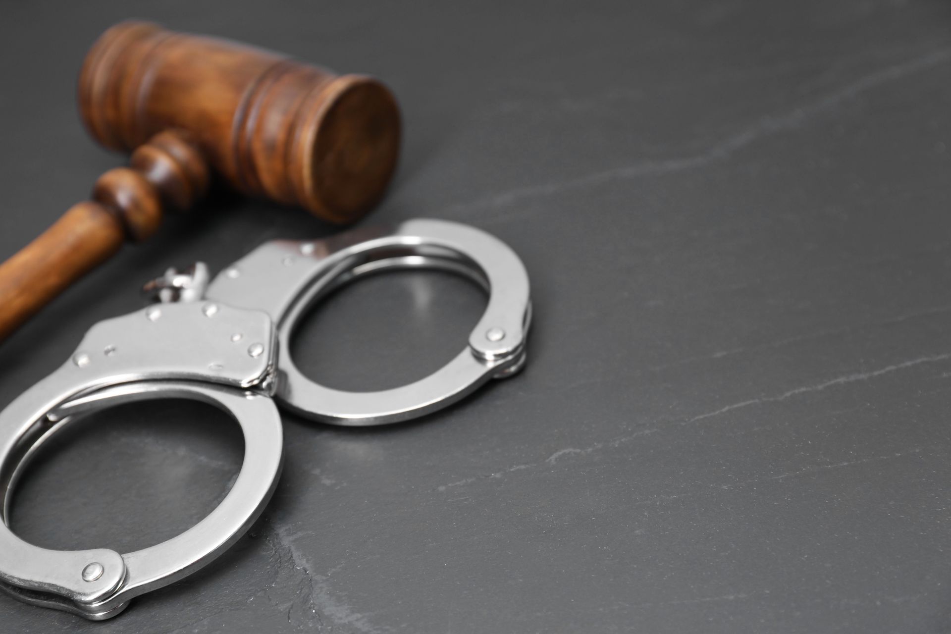 Handcuffs next to a wooden gavel on a dark gray surface.