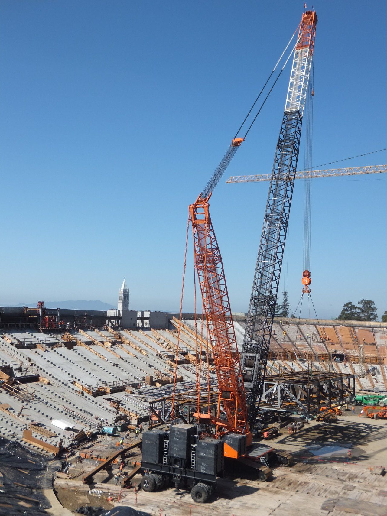 Construction site with large crane lifting materials; blue sky.