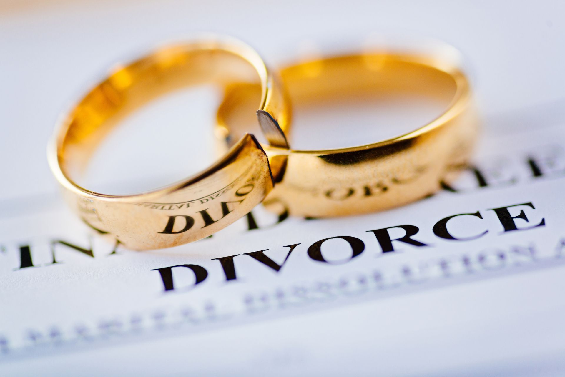 Two broken golden wedding rings and divorce decree document, representing divorce attorney services.