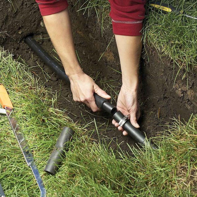 Person adjusts sprinkler watering dark stones and plants.
