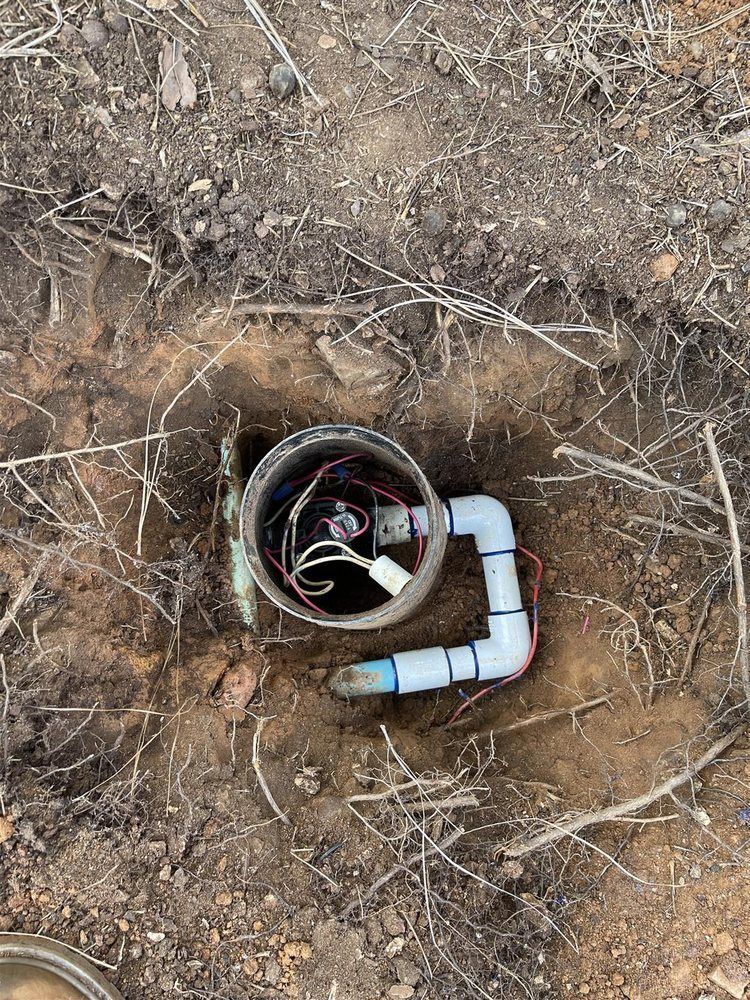 Open irrigation valve box in dirt; wires, pipes, and fittings are visible.