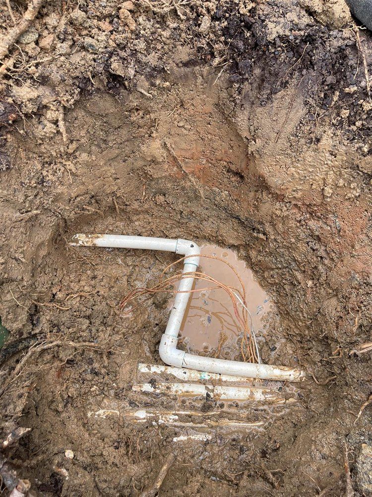White PVC pipes in a dirt hole, arranged in a Z-shape and connected to other pipes underground.
