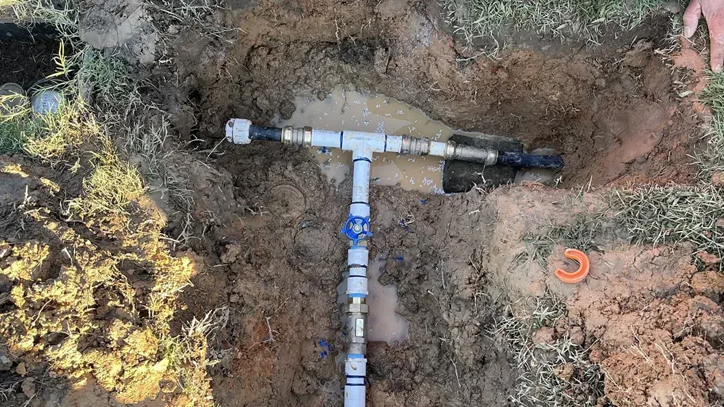 T-shaped sprinkler pipe installed underground in a patch of dirt and grass.