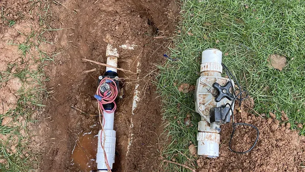Two irrigation valves are partially buried in the soil, one with wires and the other with a handle.
