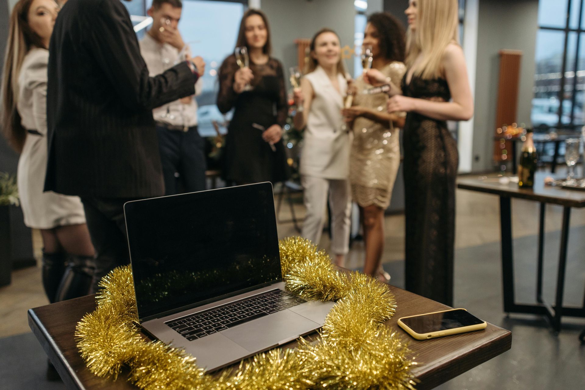 Laptop on table with tinsel, party in background.