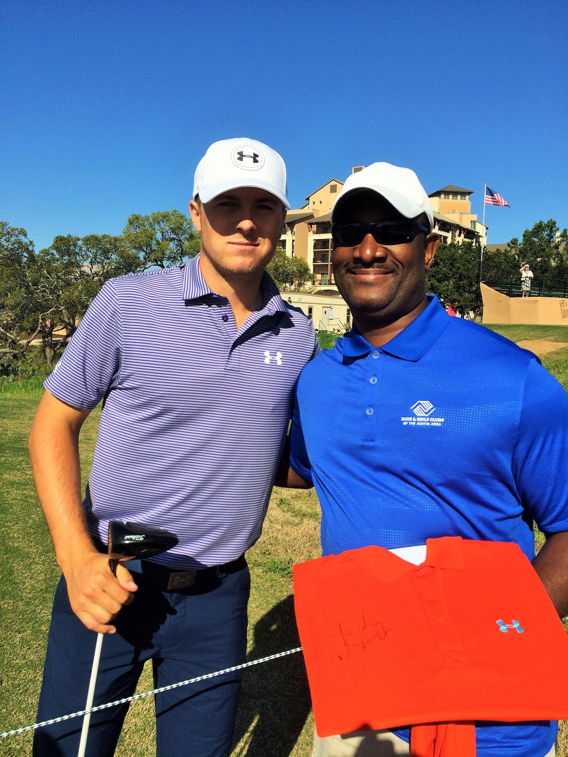 Golfer poses with a man, both wearing golf attire. They stand on a golf course under a sunny sky.