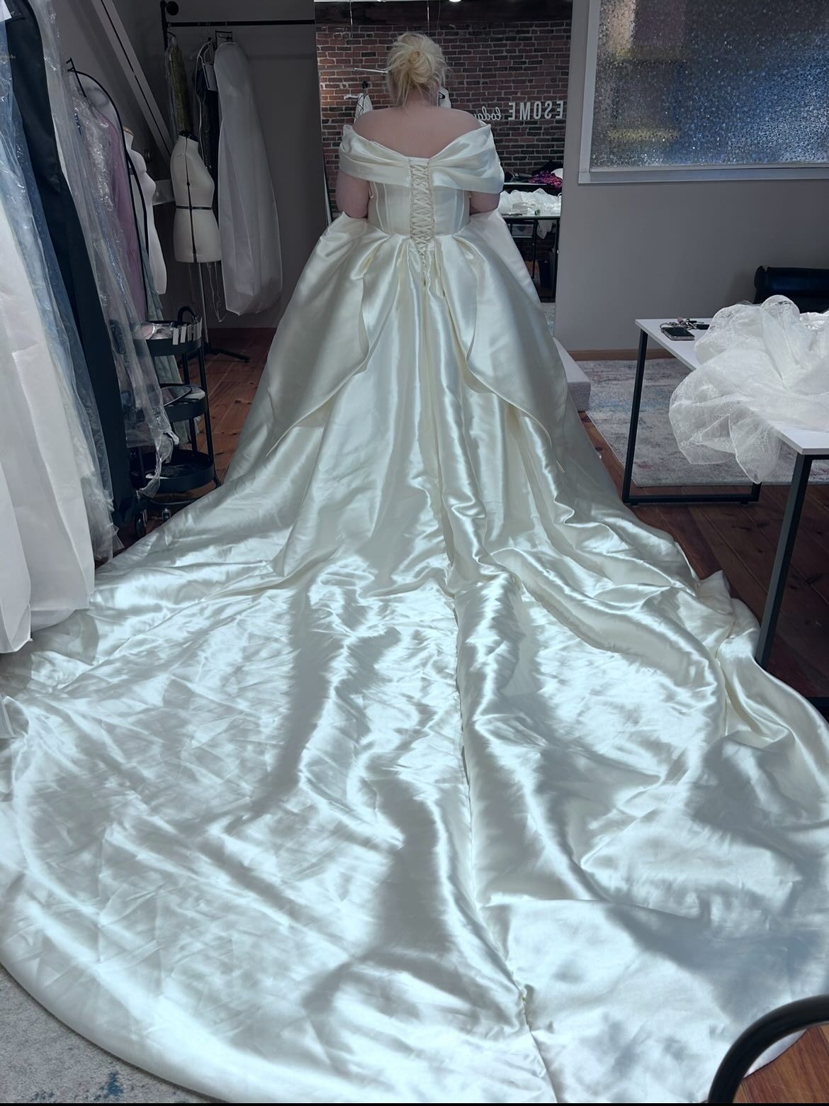 Person in a strapless white wedding gown with a long train in a dress shop mirror.