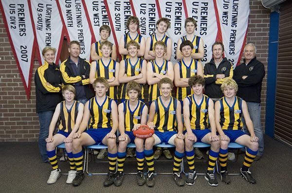 A youth Australian rules football team in yellow and black striped uniforms posing for a group photo before banners.