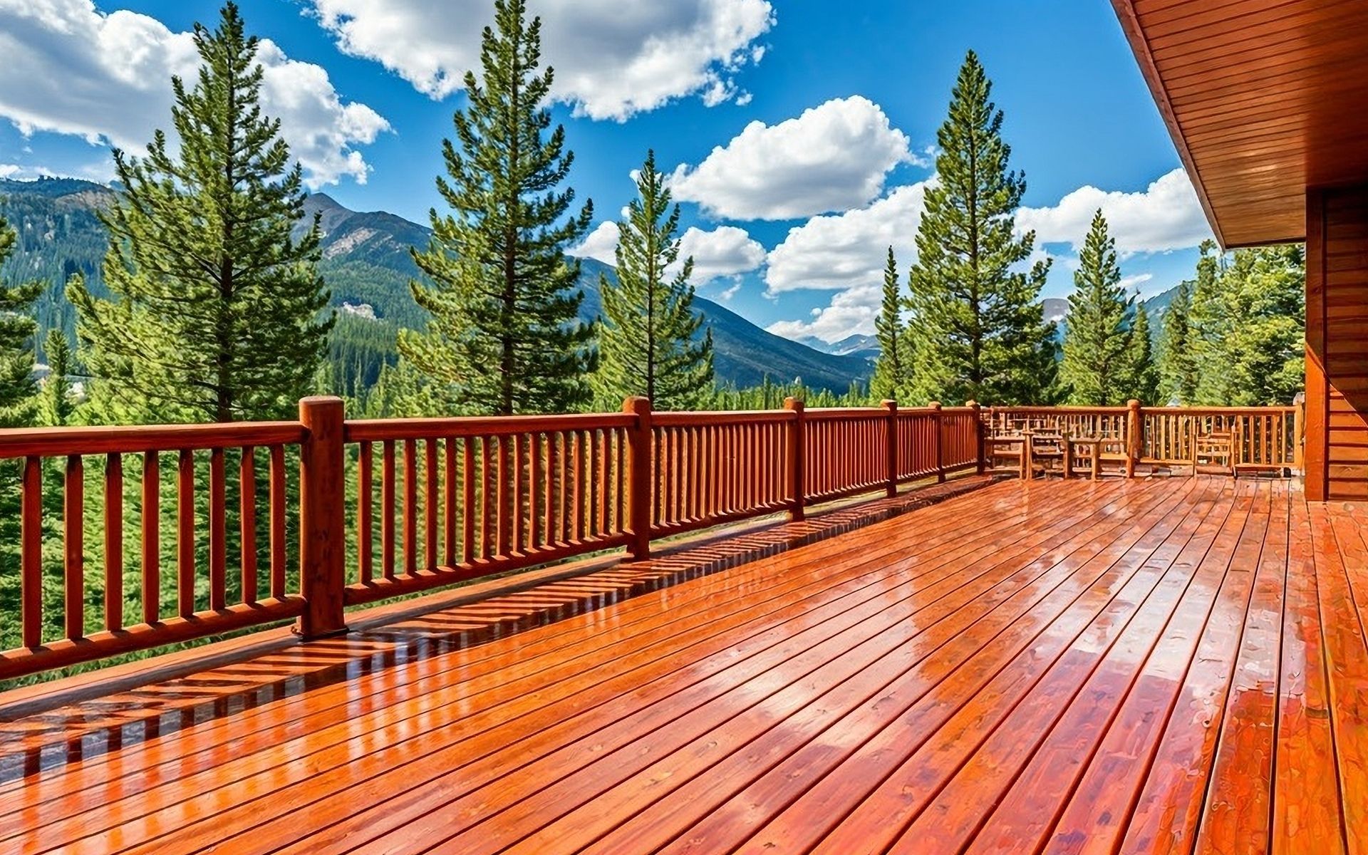 Wooden deck overlooking a mountain view, blue sky with clouds.