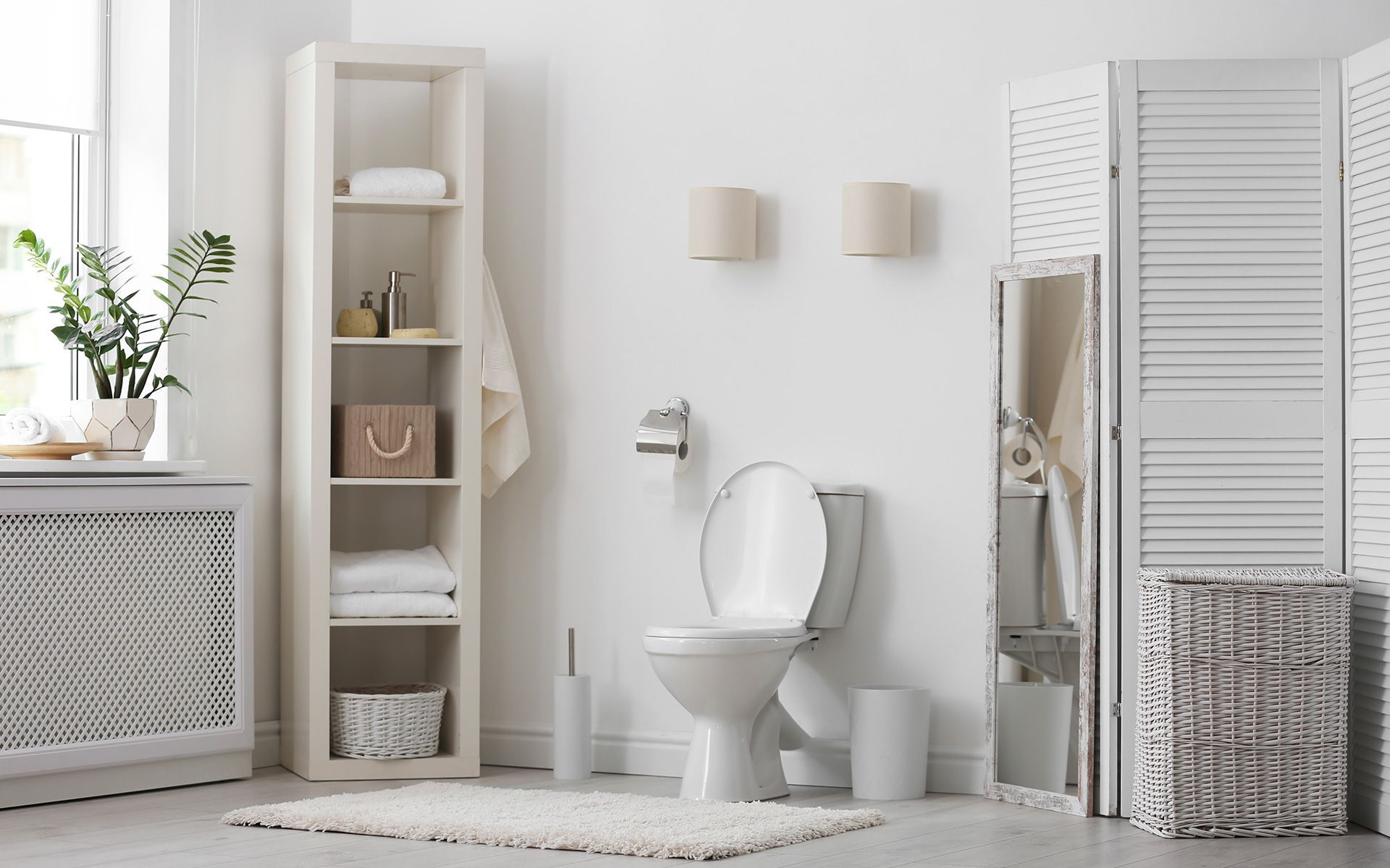 White bathroom with a toilet, shelf with towels, and decorative screen.