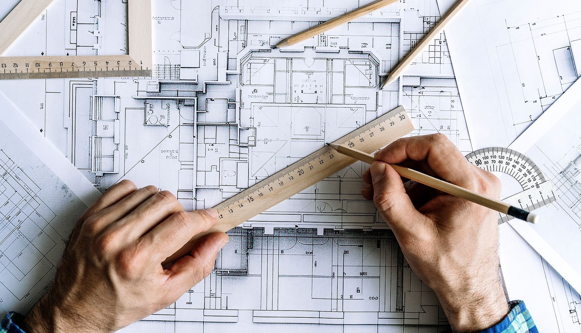 Hands using a ruler and pencil on a blueprint with other drafting tools.